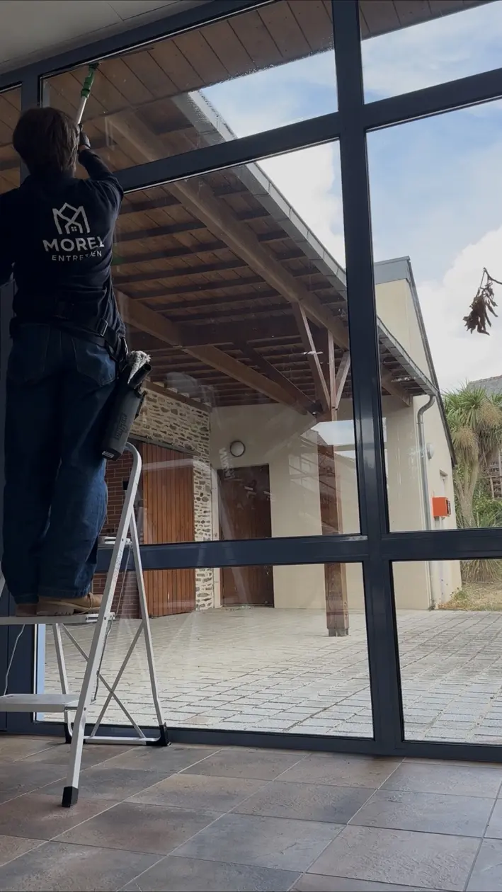 Raphaël Morel nettoie une grande baie vitrée dans des locaux professionnels
